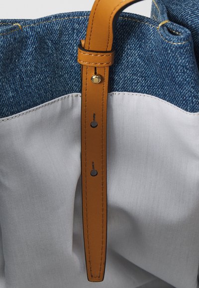 Denim and cotton shoulder bag with a tan leather strap. Features stitching details and a crisp white lower section.