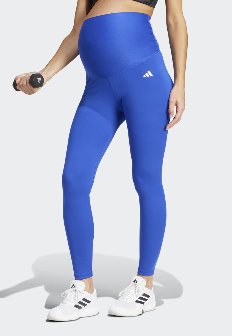 Leggings premaman blu, elasticizzati, con vita alta, texture liscia e dettaglio logo bianco. Abbinati a scarpe da ginnastica bianche.