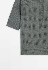 Chemise gris tricot à manches courtes avec un motif en texture gaufrée et trois boutons sur la patte de boutonnage avant, présentée à plat sur un fond blanc.