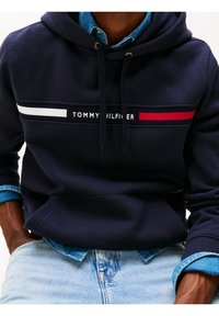 Granatowa bluza z kapturem z logo na przednim pasku w czerwono-białe paski. Miękka tkanina z kieszenią kangurką oraz regulowanym kapturem na sznurek.