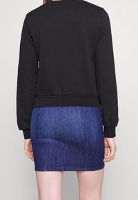 Černá mikina s dlouhými rukávy a pružnými manžetami, ve spojení s dobře padnoucími džíny sukně v tmavě modré barvě, která se vyznačuje hladkou texturou a detaily švů.