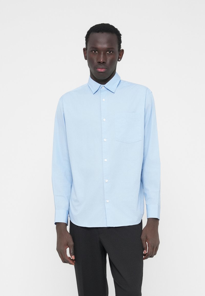 Ανοιχτό μπλε μακρυμάνικο πουκάμισο από βαμβάκι, με γιακά που κλείνει με κουμπιά, τσέπη στο στήθος και ίσια μεσοραφή. Λείο ύφασμα, απλός σχεδιασμός.
