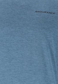 Hellblauer Stoff mit feiner Struktur und dem Wort "ENDURANCE" in kleinen, schwarzen Großbuchstaben nahe der oberen rechten Ecke gedruckt.