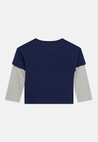 Μπλε ναυτικό κοντομάνικο τοπ με στρώση από ανοιχτό γκρι μακρυμάνικα, φαίνεται από πίσω σε λευκό φόντο.