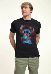 Czarna koszulka z grafiką postaci kartonowego obcego w słuchawkach, trzymającego kontroler do gier, w intensywnych kolorach niebieskim i czerwonym.