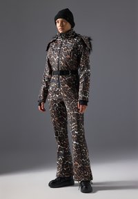 Leopardmønstret skidragt med faux fur-detaljer, tætsiddende design, lynlås foran, sort bælte og sort strikhuge, parret med kraftige sorte sko.