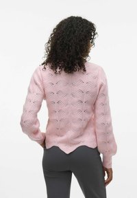 Rosa gestrickter Pullover mit einem welligen Muster, strukturiertem Stoff und gerippten Bündchen. Mit gewelltem Saum und offenen Maschenakzenten auf der Rückseite.