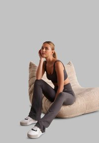 Set di abbigliamento attivo grigio a coste composto da un top corto aderente e pantaloni flared a vita alta. Abbinato a sneakers bianche su un cuscino beige testurizzato.