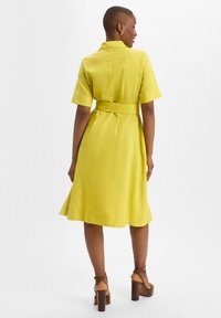 Yellow short-sleeve dress with a collar, cinched waist, full skirt, and a smooth texture. Paired with brown heeled sandals.