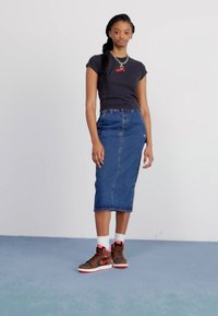 Black fitted t-shirt with red text, blue denim midi skirt, and brown high-top sneakers with red accents and white socks. Plain background.