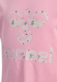 Roze katoenen T-shirt met een groot, bloemenpatroon logo en tekst, met een gladde structuur en contrasterende kleuren.