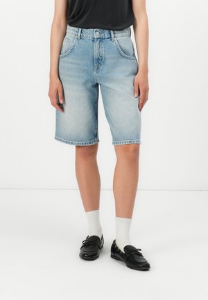 Lys blå denim shorts med en avslappet passform, fem lommer og råkant. Kombinert med svarte sko og hvite ankelsokker.
