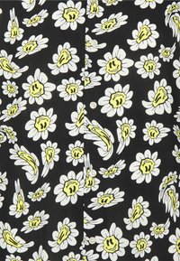 Chemise en tissu noir présentant un motif de marguerites blanches au centre jaune. Des boutons sont visibles sur le devant, créant un design classique.