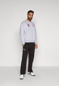 Sweatshirt cinzenta com emblema bordado e número 10. Calças de treino pretas com logótipo "Ser", usadas com ténis brancos.