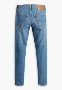 Jean en denim bleu avec jambes droites, deux poches arrière, passants de ceinture et un patch en cuir marron avec la marque sur la ceinture.