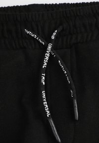 Czarne dresy z teksturowanym, elastycznym paskiem w talii z sznurkiem do regulacji. Sznurek ma biały nadrukowany tekst do dopasowania.