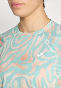 Camisa atlética ligera en aqua con un patrón abstracto en coral, con un escote redondo y un pequeño logo blanco en el pecho.