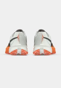 Fehér és szürke sportcipők narancssárga részletekkel, texturált hálós felsőrésszel, támogató sarokrésszel és masszív talppal.