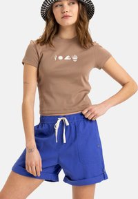 Brun bomulls-t-shirt med vita grafik, i kombination med blå shorts med elastisk midja och uppvikta ärmar.