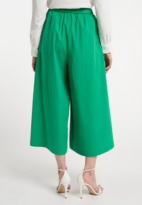 Groene culottes met een elastische tailleband, gemaakt van een gladde stof. Heeft een brede, cropped pootsilhouet. Gemaakt met witte hoge hakken sandalen.
