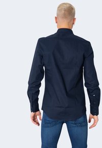 Camicia a maniche lunghe blu navy con colletto a bottoni, cucitura del dietro e polsini con bottoni. Realizzata in tessuto liscio, vestibilità aderente, design elegante.