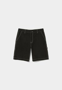 Mustat farkkushortit, joissa on valkoinen ompelu, kaksi etutaskua ja yksi sivu-tasku, jossa on merkki. Säännöllinen istuvuus ja polven puoliväliin ulottuva pituus.