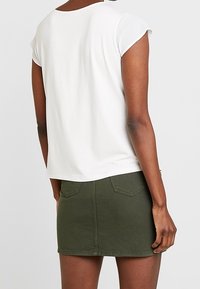 Vit kortärmad topp som matchas med en olivgrön denimkjol. Toppen har en rundad halslinning; kjolen har bakfickor och en figurnära silhuett.