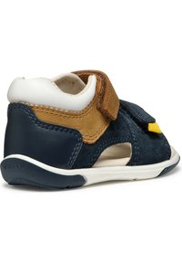 Zapato de cuero para niño pequeño en navy y marrón, con correa de velcro, acentos de ante, perforaciones para ventilación y suela de goma blanca. Presenta un logo en el talón.