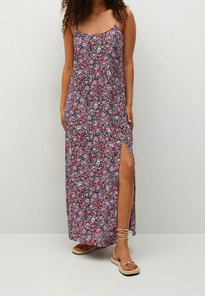 Femme portant une robe longue sans manches à fleurs roses et violettes avec une fente haute, associée à des sandales beige à lacets.