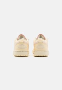 Sneakers color crema con dettagli in rosa chiaro. Caratteristiche includono una texture liscia, logo ricamato sul tallone e suola in gomma.