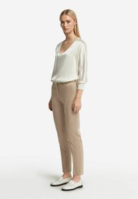 Silkig vit blus med V-hals och trekvartslånga ärmar, kombinerad med beigefärgade slim-fit byxor och vita loafers med svarta sulor.