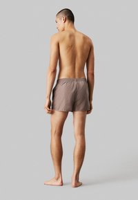 Pantaloni da bagno marroni da uomo con vita elastica, realizzati in materiale leggero, caratterizzati da un design semplice e senza motivi o dettagli visibili.