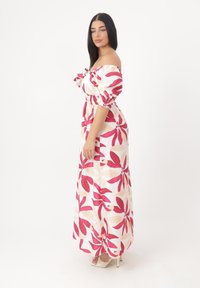 Robe maxi avec un design décolleté, motif floral rouge et crème, ceinture élastique et tissu fluide avec une texture douce.