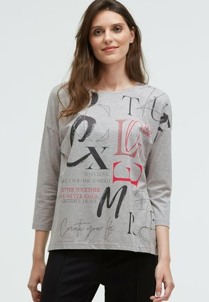 Graues Langarmshirt mit unterschiedlichen schwarzen und roten Textgrafiken, einschließlich Phrasen und Buchstaben, locker geschnitten und mit Rundhalsausschnitt.