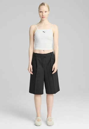 Witte geribbelde crop top met dunne bandjes, gecombineerd met zwarte geplooide wijde shorts. De schoenen zijn lichte grijze instappers.