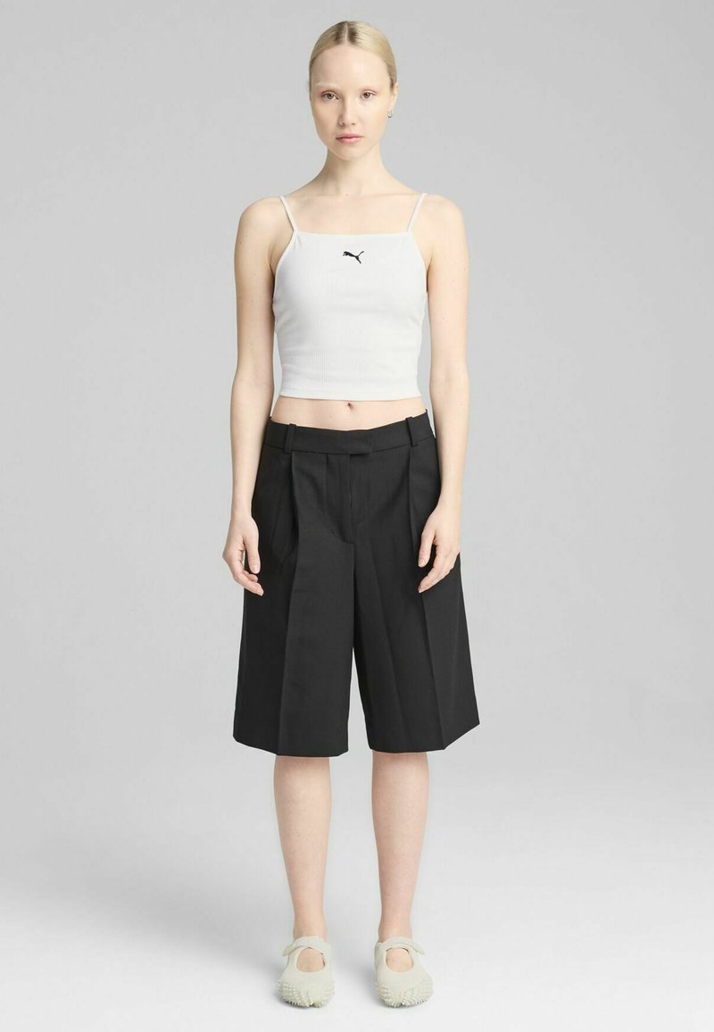 Hvid ribbet crop top med tynde stropper, parret med sorte plisserede vide shorts. Skoene er lysegrå slip-on sko.