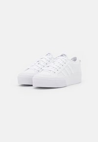 Vita sneakers med en texturerad gummisula, snörning och perforerade sidopaneler. Har tre ränder på utsidan.