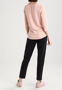 Jasnoróżowa, teksturowana bluzka z rękawami do połowy przedramienia i zamkiem z tyłu; zestawiona z czarnymi, zwężanymi spodniami i jasnoróżowymi trampkami.