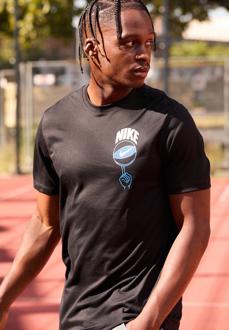Schwarzes Nike T-Shirt mit blauem Grafikdesign eines Basketballs und einer Hand auf der Vorderseite. Kurze Ärmel, glattes Material, taillierte Passform.