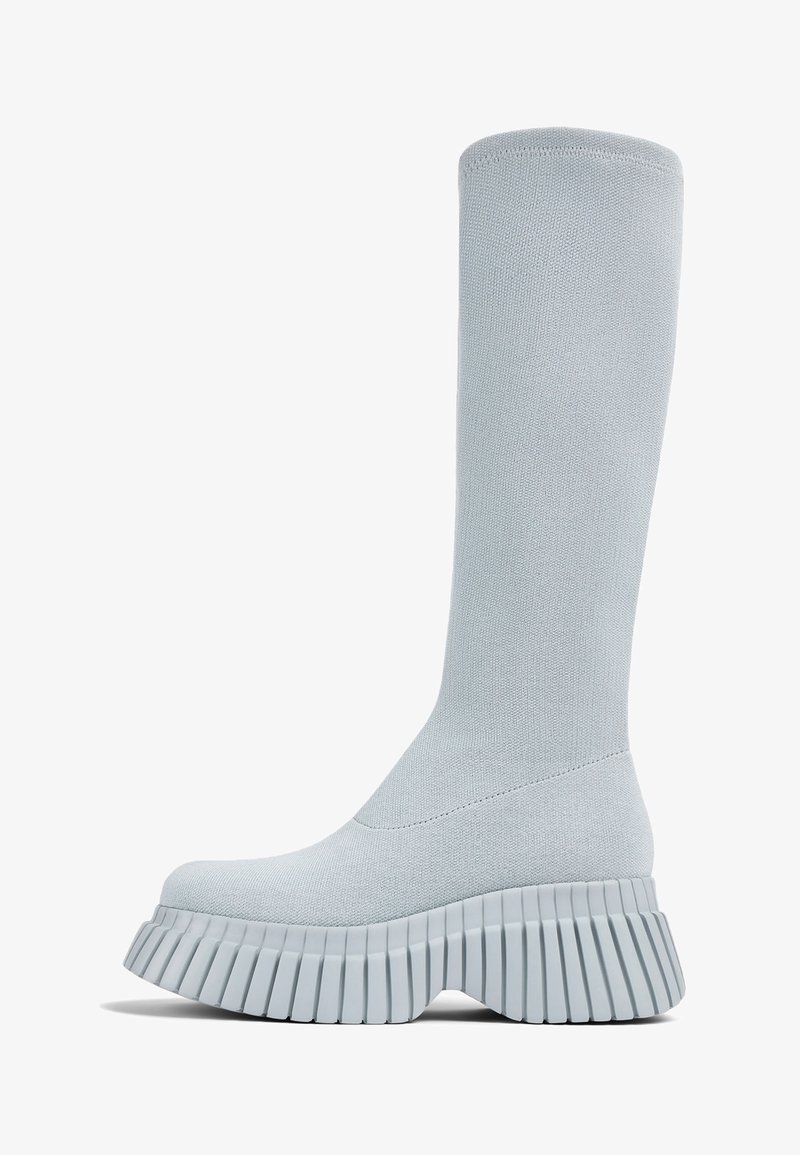 Bottes montantes grises claires en tissu extensible avec une semelle plateforme épaisse côtelée. Texture lisse, design minimaliste.