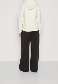 Krämfärgad luvtröja med avslappnad passform, med ribbade muddar och fåll. Matchas med svarta vida byxor i ett strukturerat tyg.