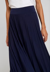 Gonna plissettata blu navy con vita larga e design fluido, realizzata in un tessuto leggero, presenta dettagli di trama verticale.