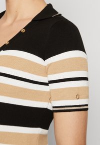 Maglia polo lavorata a maglia con righe orizzontali nere, bianche e beige. Accentuata da bottoni dorati e un piccolo logo "G" sulla manica.