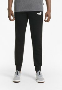 Svarta sweatpants med ribbade muddar, med en vit Puma-logotyp på vänstra låret. Tillverkade av mjukt, strukturerat material.