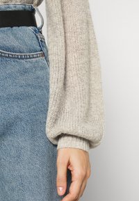 Knitted light beige sweater with balloon sleeves, paired with mid-rise blue denim jeans and a black belt, showcasing a textured fabric.