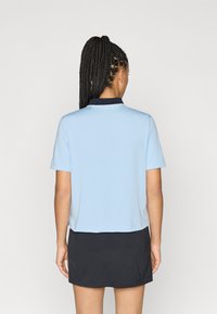 Svijetloplava polo majica s kratkim rukavima, s tamnoplavim ovratnikom. Uparođena s crnom suknjom. Glatka tkanina i jednostavan dizajn.