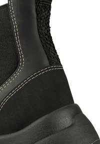 Czarny bucik z teksturowanej tkaniny i gładkiej skóry, z kontrastującymi białymi szwami oraz solidną gumową podeszwą.