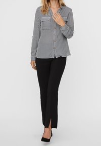 Camicia a righe bianca e nera con bottoni, dotata di due tasche sul petto. Abbinata a pantaloni neri con fessure laterali all'orlo.