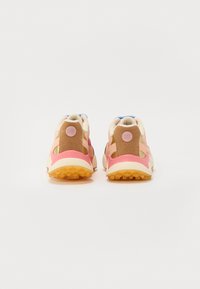 Sportssko med en blanding af pink, tan og hvide materialer; sok-lignende konstruktion med en tekstureret sål og logo detalje bagpå.