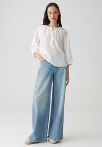 Top bianco in lino con scollatura rotonda e dettagli con lacci, abbinato a jeans in denim azzurro chiaro a gamba larga, caratterizzati da una vestibilità morbida e orli sfrangiati.